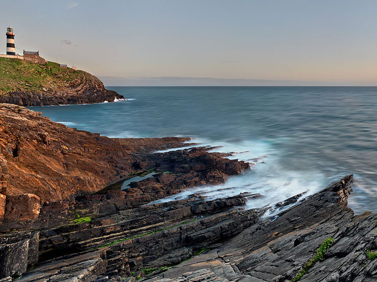 Sunset over the Old Head lighthouse in County Cork with Atlantic waves rolling against the cliffs