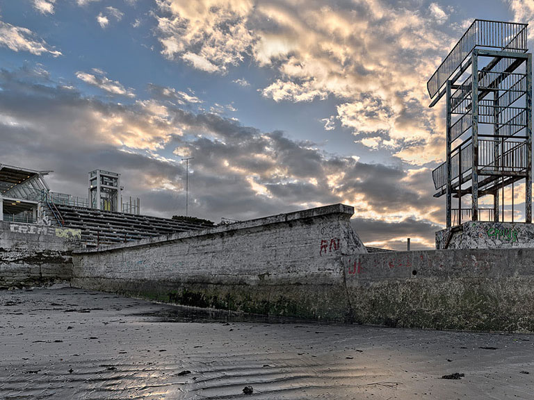 Graffitied concrete walls and empty pool at the abandoned Blackrock Baths in Dublin, with sea and sky beyond