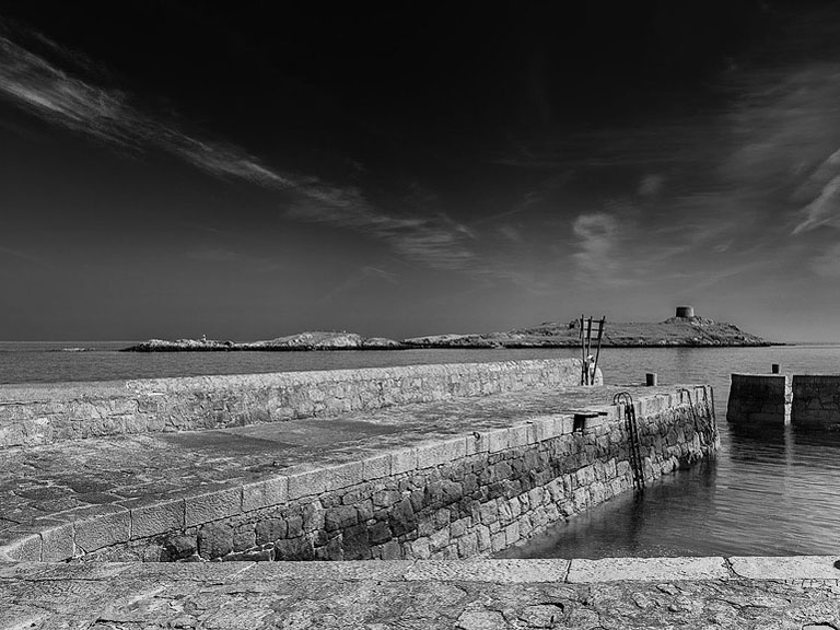Black and white photograph of Coliemore Harbour in Dalkey with boats, harbour walls and Dalkey Island beyond