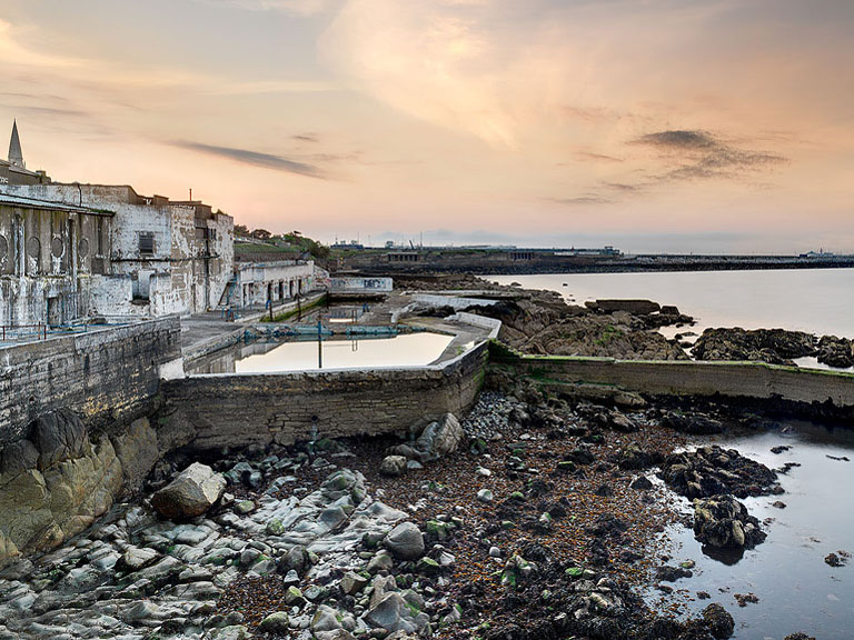 Dun Laoghaire Baths at sunset with pool, promenade and glowing sky over Dublin Bay