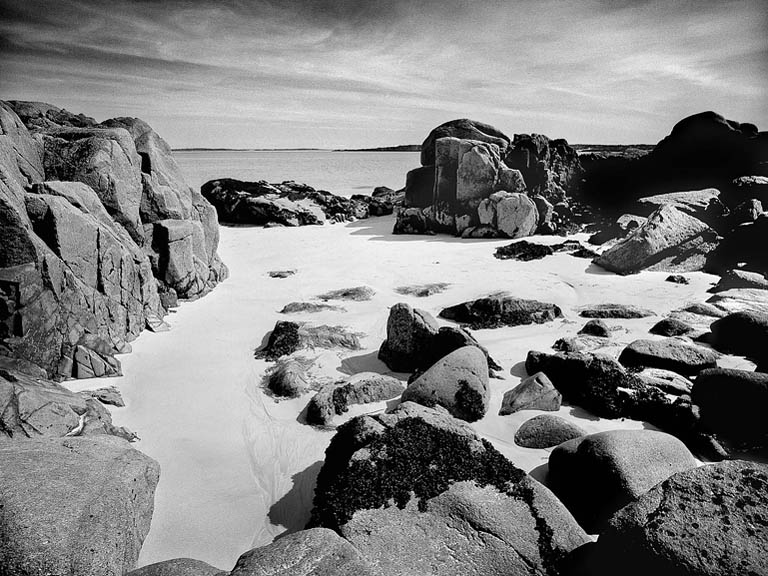 Black and white photograph of Gurteen Beach near Roundstone in County Galway, showing smooth stones, open sand and the Atlantic Ocean.