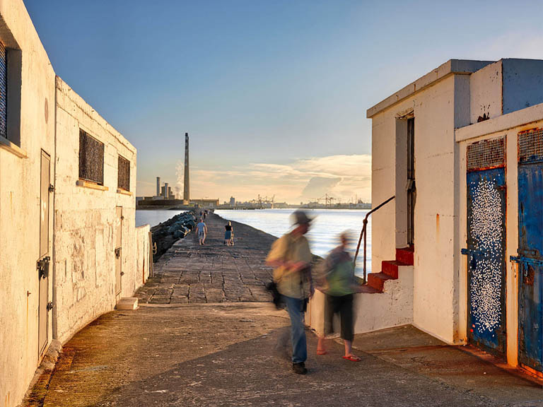 Fine art photograph of the Half Moon Swimming Club house on the South Wall in Dublin Bay, with sea, concrete pier and railings in soft evening light.