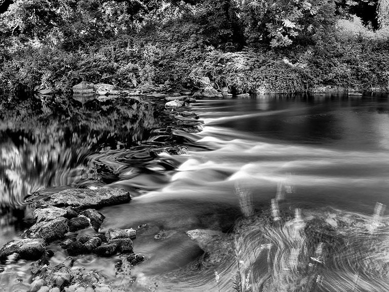 Photograph of the River Slaney flowing through Altamont Gardens in County Carlow, with trees, rocky banks and reflections on the water.