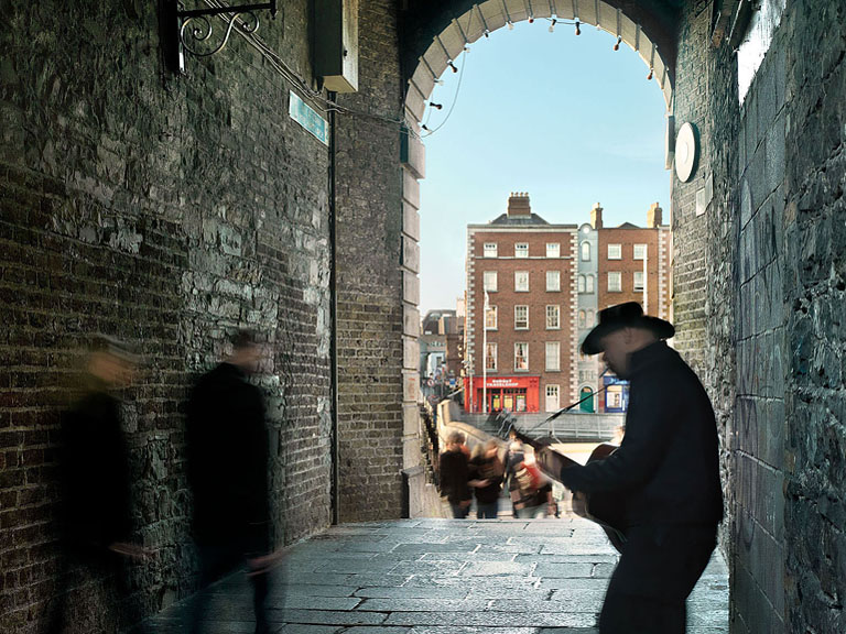 Fine art photograph of a street busker playing under Merchants Arch in Dublin, with stone walls, archway and passing pedestrians.