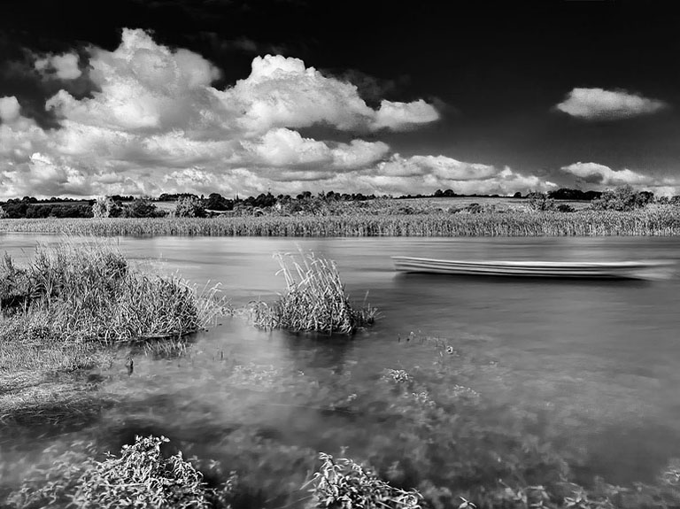 Fine art photograph of a small moored boat on the River Slaney in County Carlow, with reeds, trees and reflections on the water.