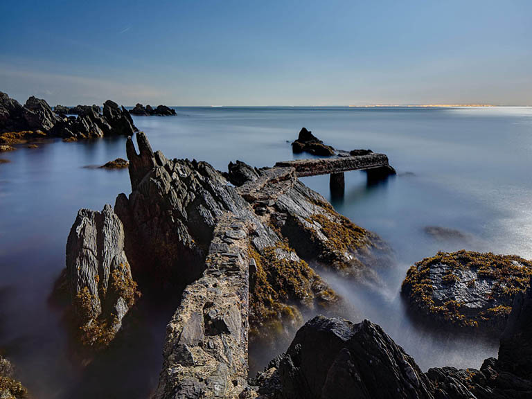 Night time photograph of Shroove Pier on the Donegal coast, with stone pier, harbour lights and dark water under a moonlit sky.