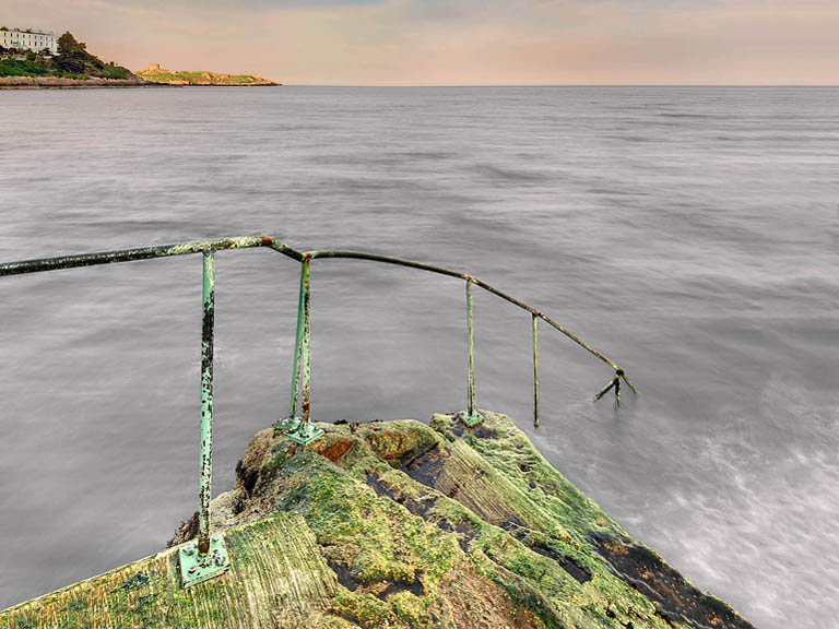 Sunset seascape from the Vico Baths looking towards Dalkey Island in Dublin, with glowing sky and calm sea