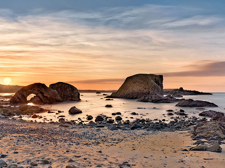 Seascape photograph of Ballintoy Arch on the County Antrim coast with waves breaking against rugged rocks.