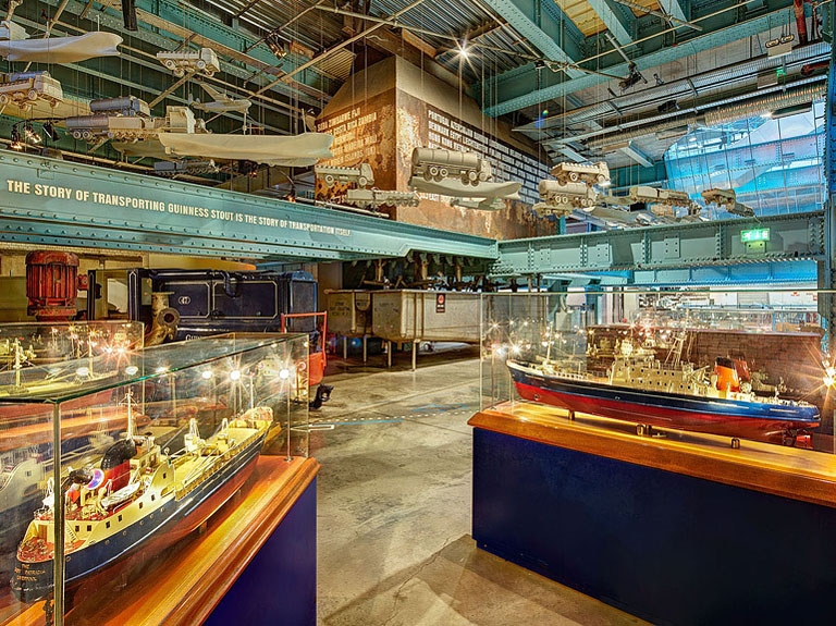 Display of boat models in glass cases inside the Guinness Storehouse with warm light and reflections.