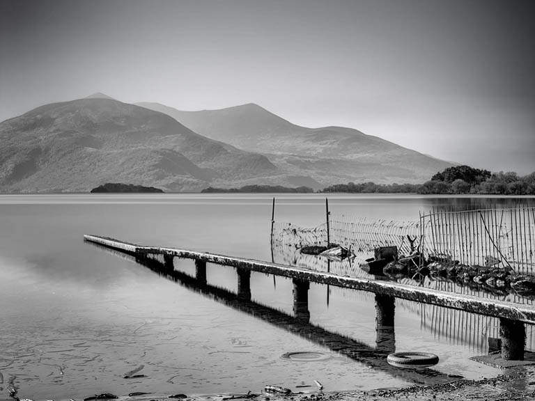 Long exposure black and white photograph of Lough Leane in Killarney, County Kerry, showing calm water and shoreline structure