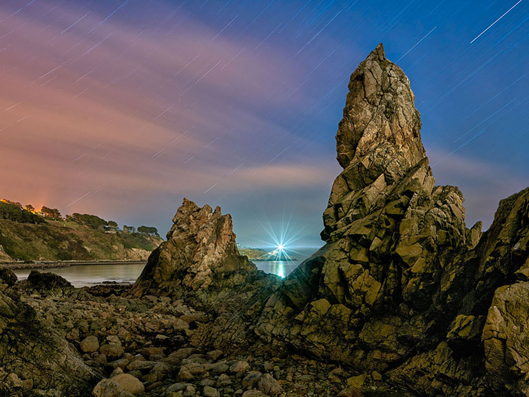 Night photograph of Baily Lighthouse on Howth Head, Dublin, with star trails above rocky coastline