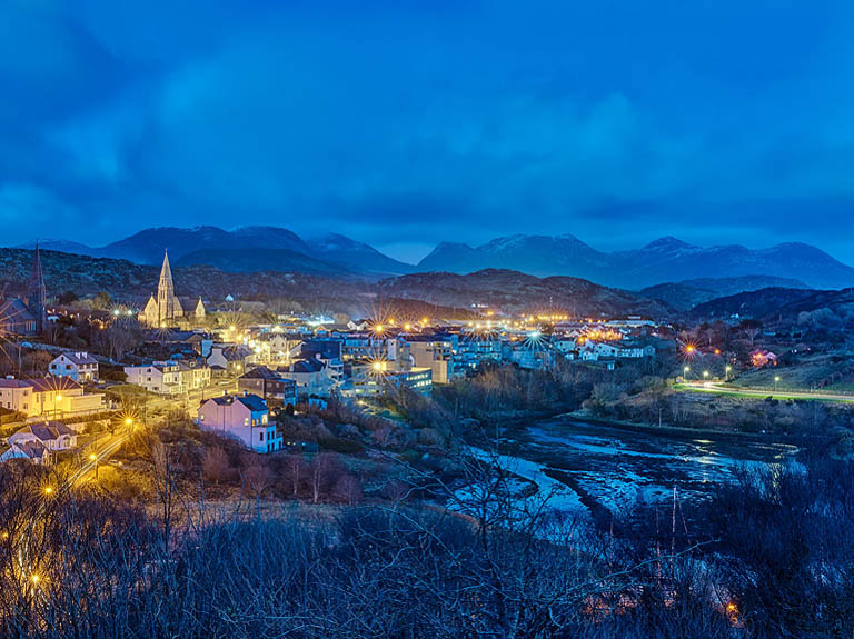 Night photograph of Clifden in County Galway at dusk, showing town lights and roads through the Connemara landscape