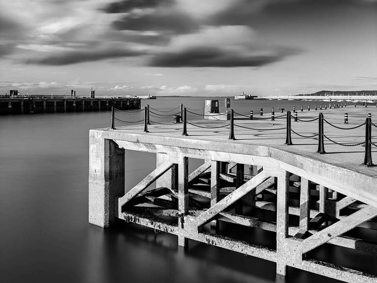 Long exposure photograph of Dun Laoghaire Pier at low tide in Dublin Bay, with softened sea and moving clouds