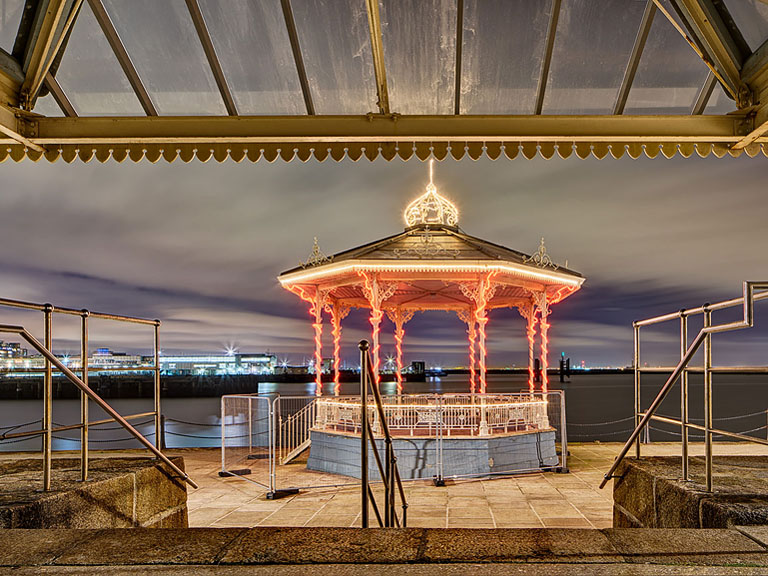 Night photograph of the bandstand and sun shelter on Dun Laoghaire Pier in Dublin, lit by Christmas lights and street lighting