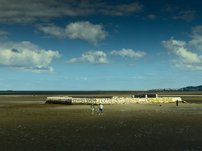 Square photograph of Sandymount Strand in Dublin at low tide, with wide sand flats and distant headlands across the bay.