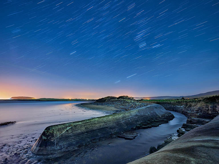 Astrophotography view of Dunmoran Beach in County Sligo at night, with waves breaking under a clear star filled sky.