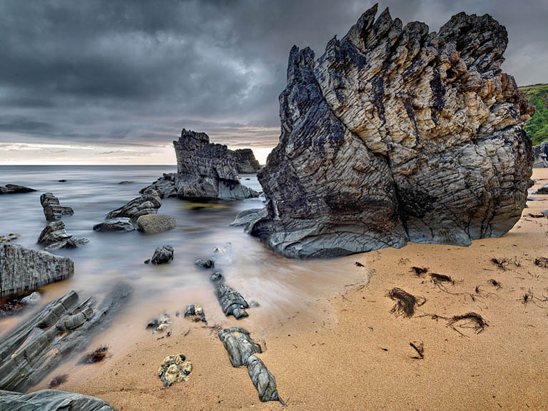 Kylemore Abbey in Connemara reflected in the calm surface of the adjoining lake with wooded hills behind.