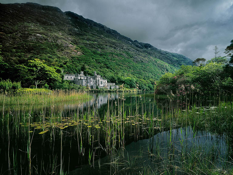 Fine art photograph of Kylemore Abbey reflected in the lake, surrounded by trees and mountains in the Connemara landscape in County Galway