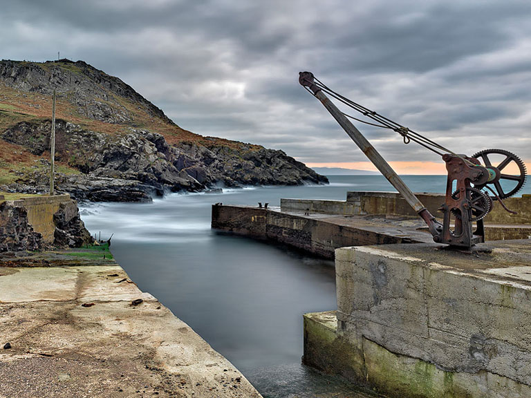 Vintage toned seascape photograph of Port Aleen Bay on the Antrim coast, with rocks in the foreground and distant headlands