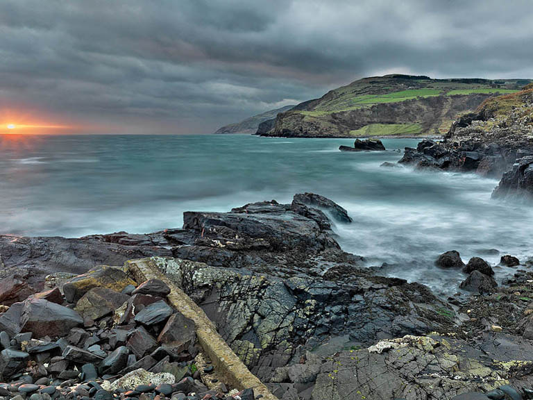 Sunrise seascape photograph of waves breaking around rocks at Port Aleen Bay on the Antrim coast with soft early light on the horizon